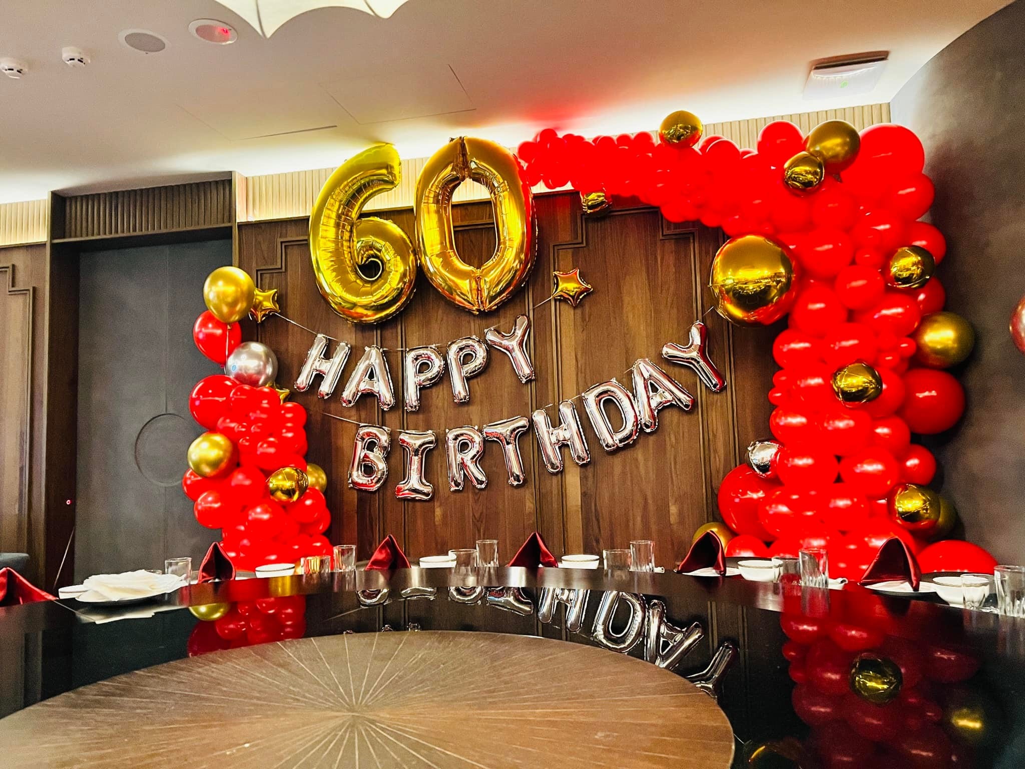 六十大壽紅金包廂佈置全景，大圓桌後方是紅色氣球拱與 HAPPY BIRTHDAY