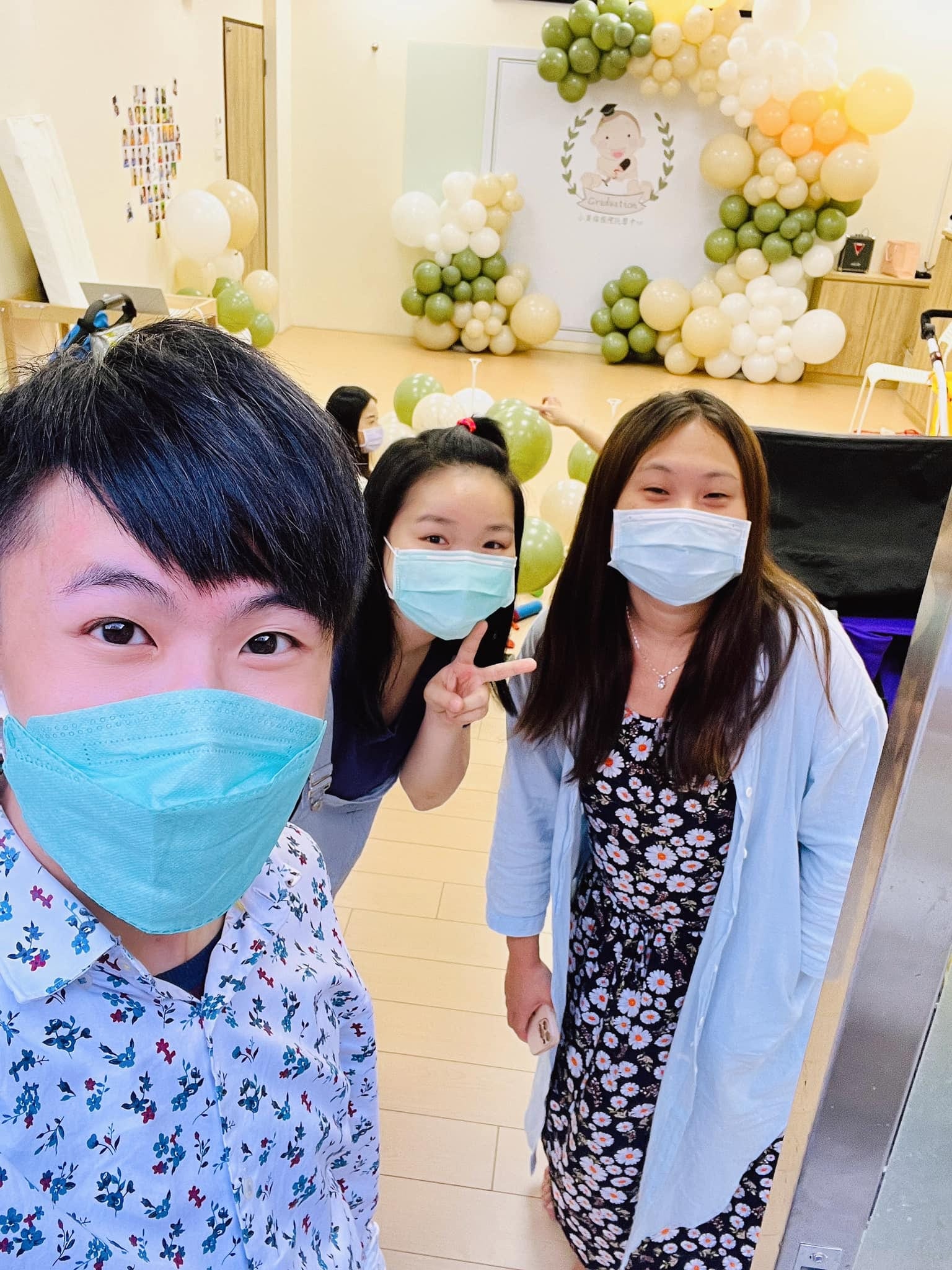 柯男與兩位老師在托嬰中心自拍，後方是畢業拍照區