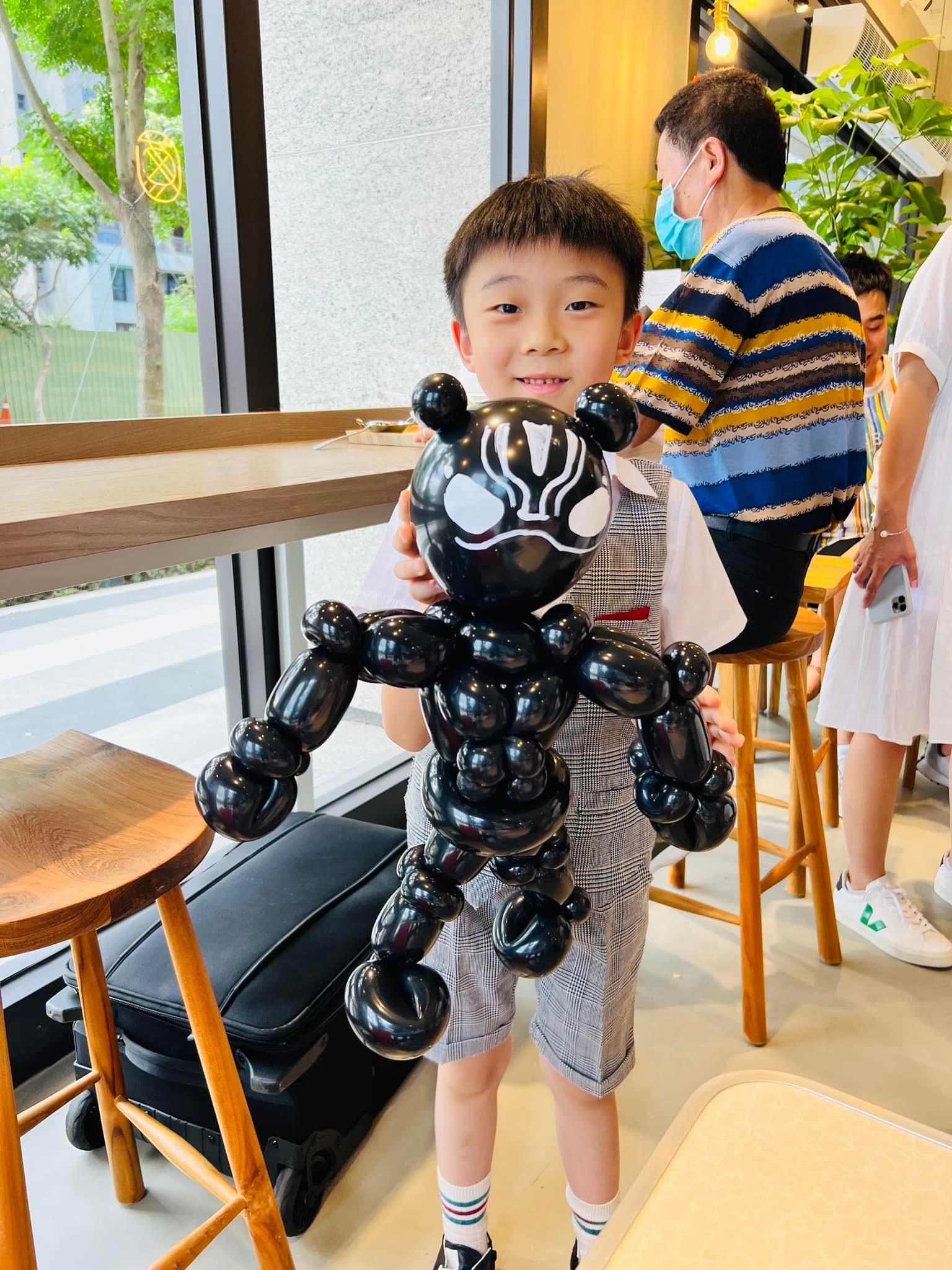 穿格紋衣服的男孩抱著全身黑色、臉上有銀色線條的英雄造型氣球
