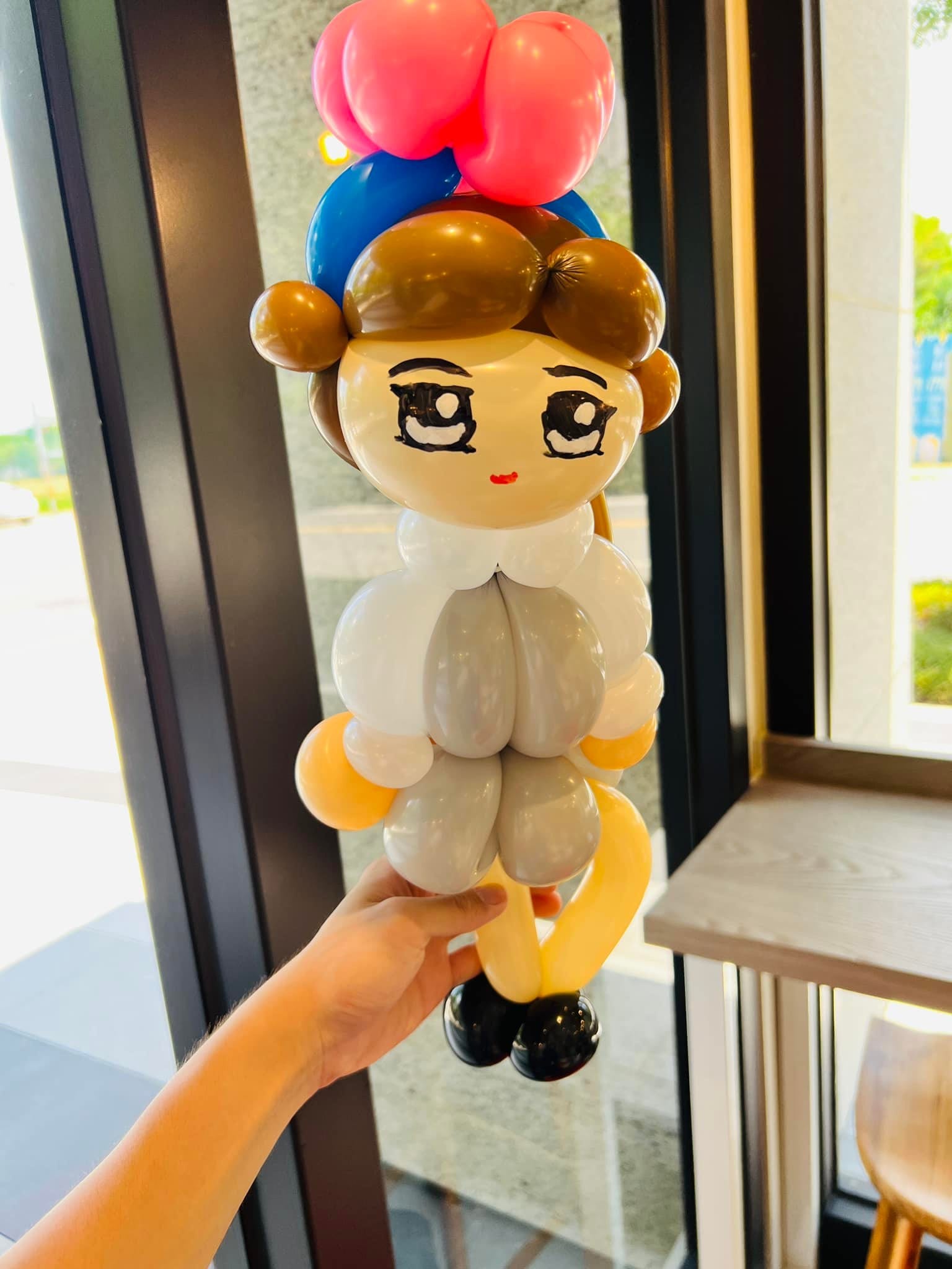咖啡色短髮、白色衣服的女生造型氣球，頭上綁著紅藍色蝴蝶結