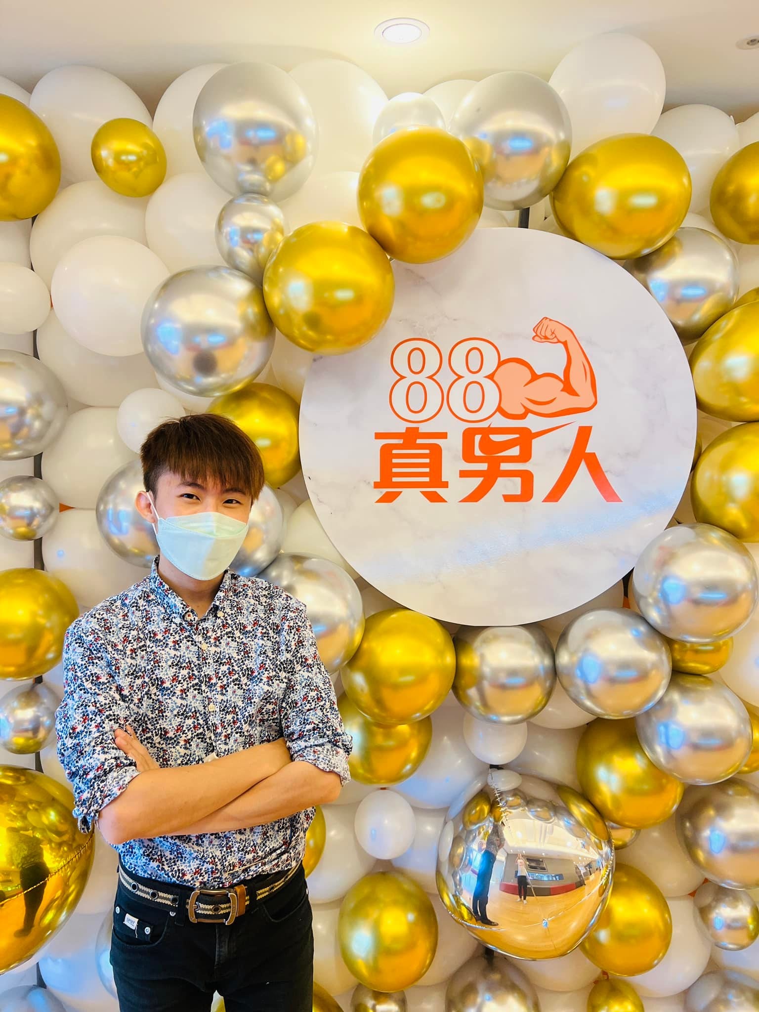 柯男站在金銀白氣球牆前，旁邊是 88 真男人主題圓牌