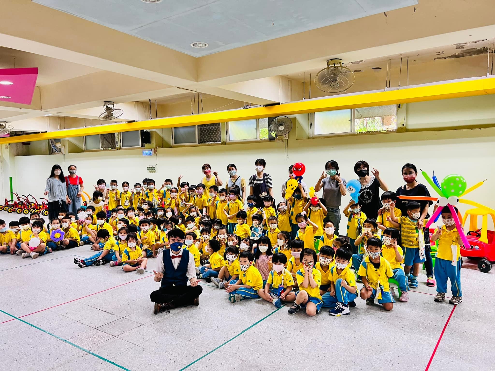 幼兒園禮堂裡，柯男盤腿坐在最前排，和一大群黃衣孩子合照
