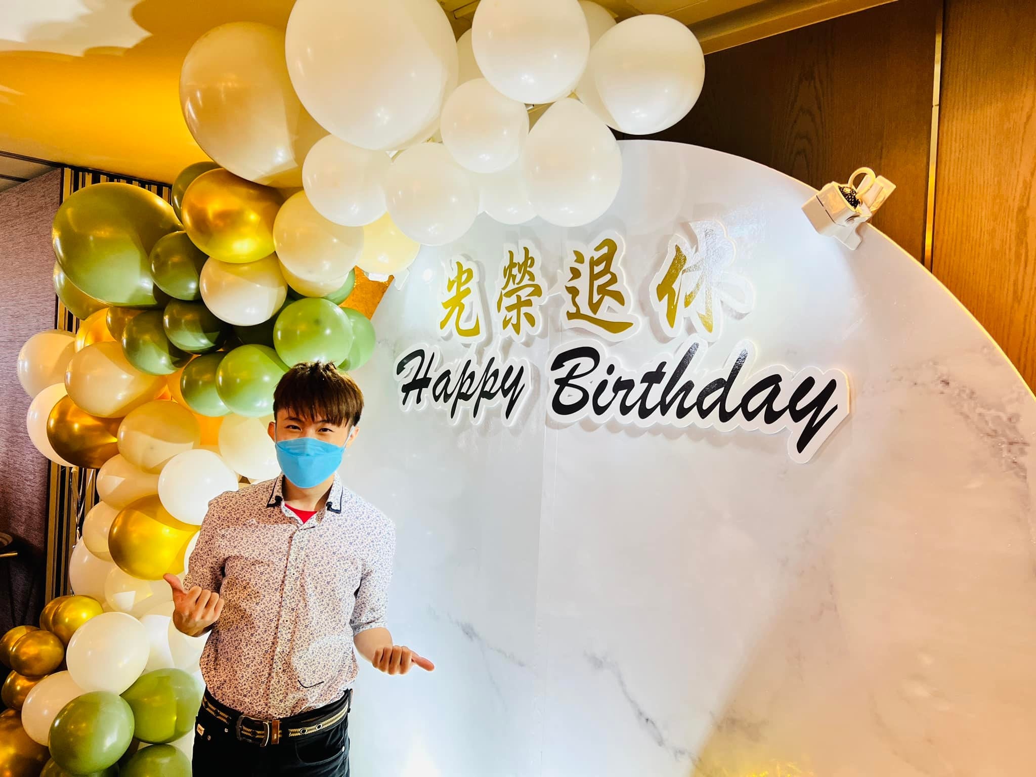 柯男站在寫著光榮退休與 Happy Birthday 的白色大理石紋背板前