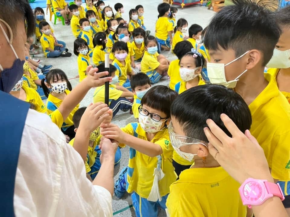 穿黃色園服的孩子們伸手摸柯男手上的黑色魔術棒