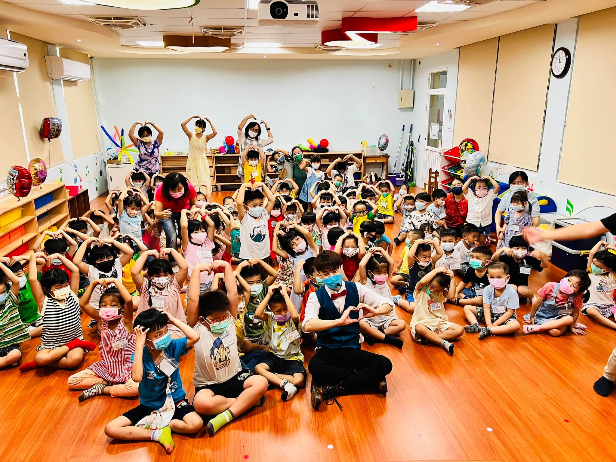 忠貞附幼教室裡，孩子們坐在木地板上和柯男一起比愛心合照