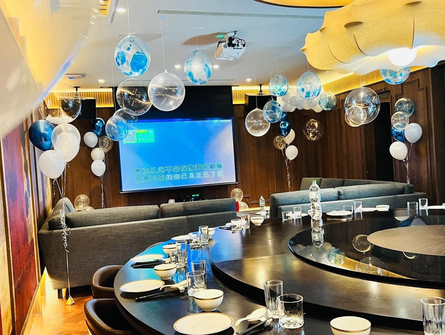 包廂大圓桌擺好餐具，天花板與牆邊都是藍白空飄氣球