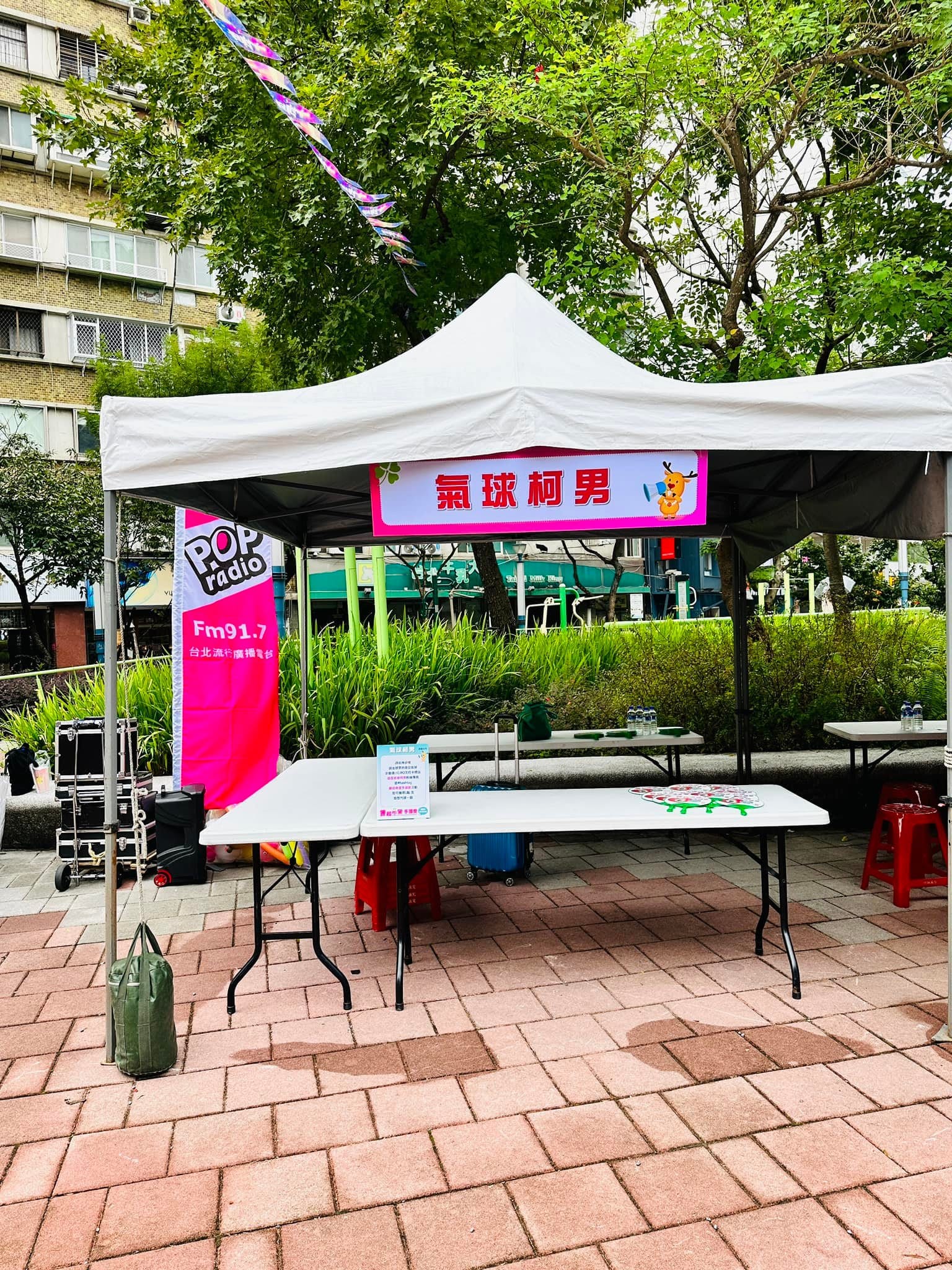公園裡的白色帳篷掛著氣球柯男布條,旁邊立著 POP Radio 旗幟