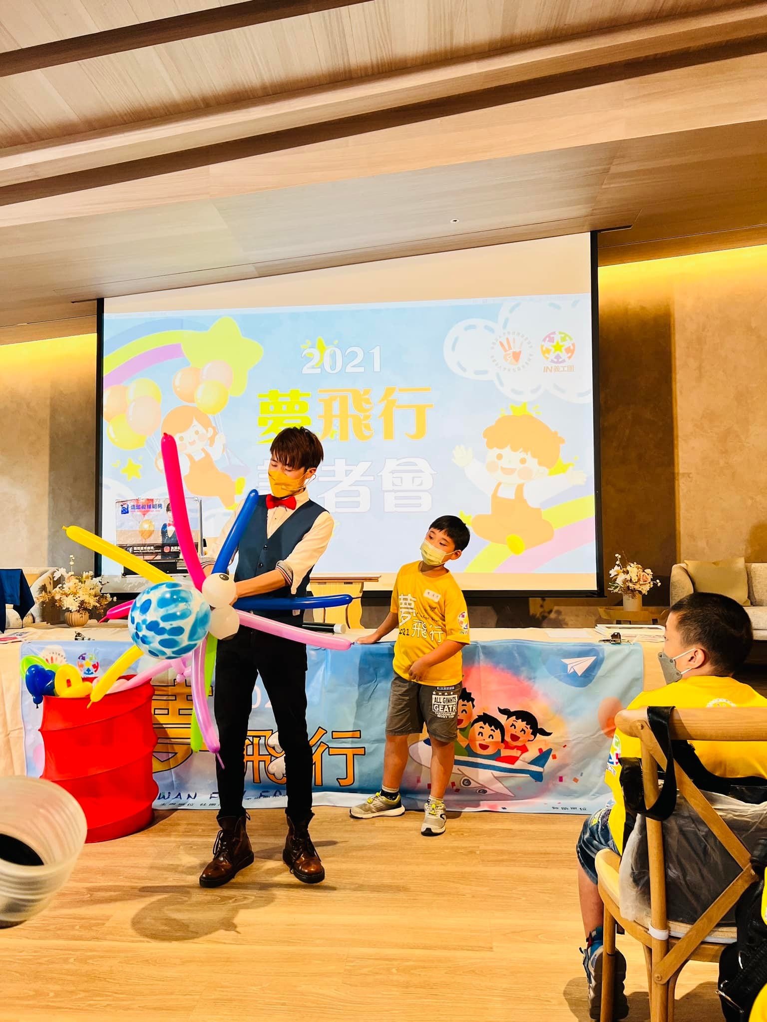 柯男拿著插滿長條氣球的大球，和上台的小男孩一起完成氣球魔術