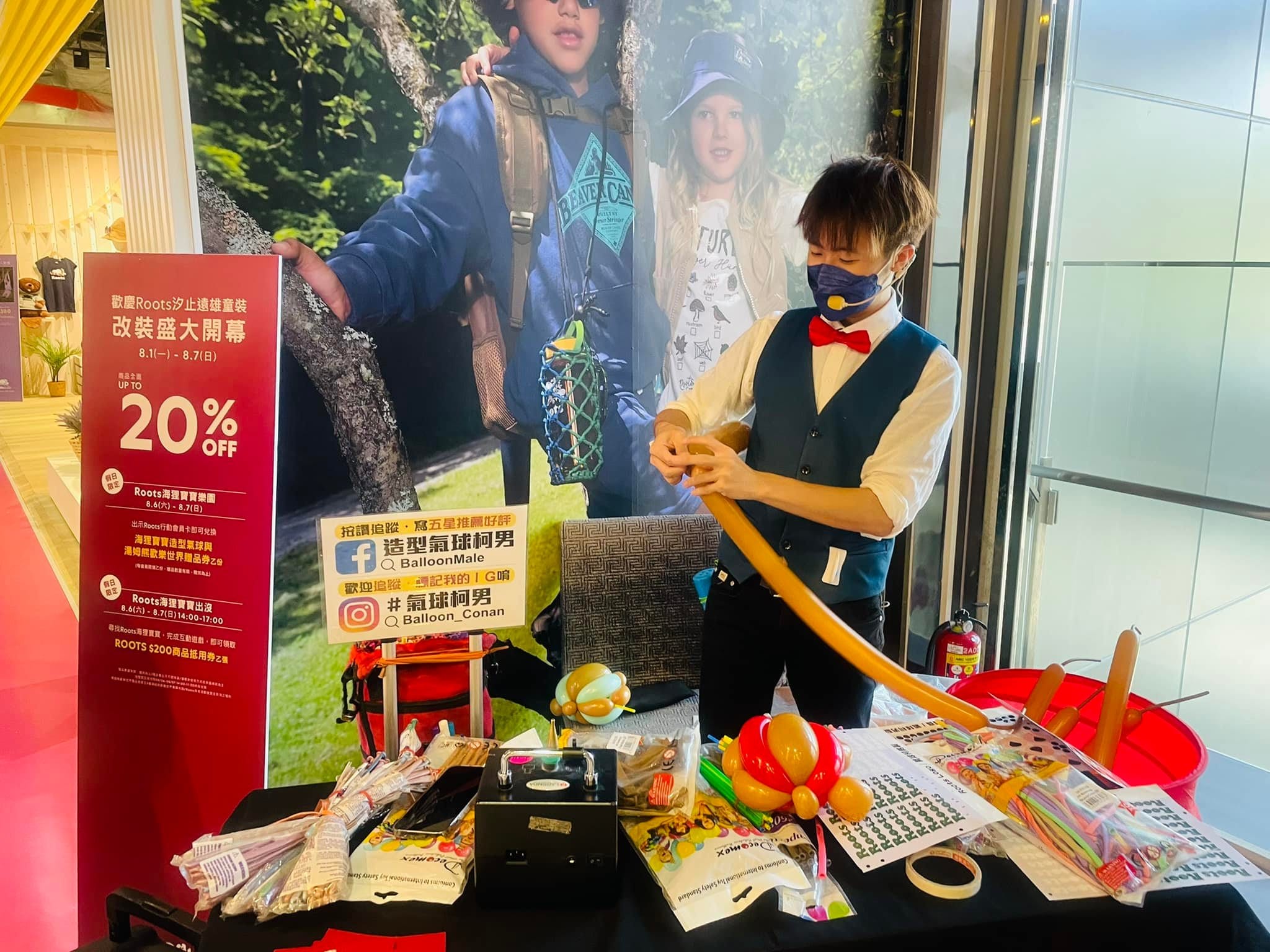 柯男在 RootsKids 海報前的長桌折咖啡色長條氣球