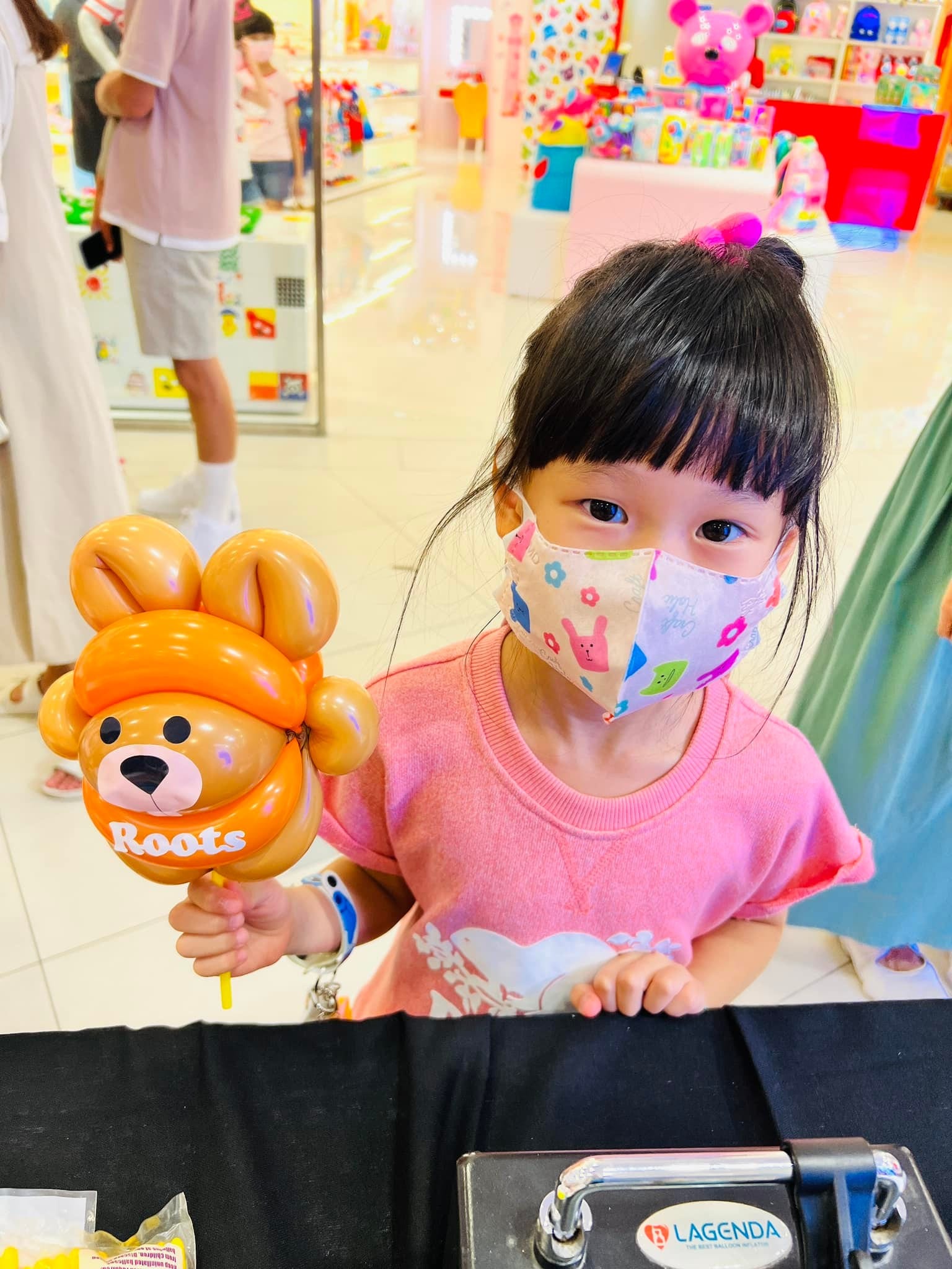 穿粉紅上衣的小女孩在攤位前拿著橘色海狸寶寶氣球