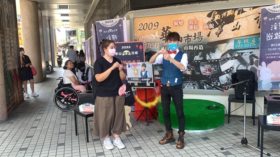 騎樓舞台上,柯男和穿黑衣的女士一起拿著粉紅色道具表演