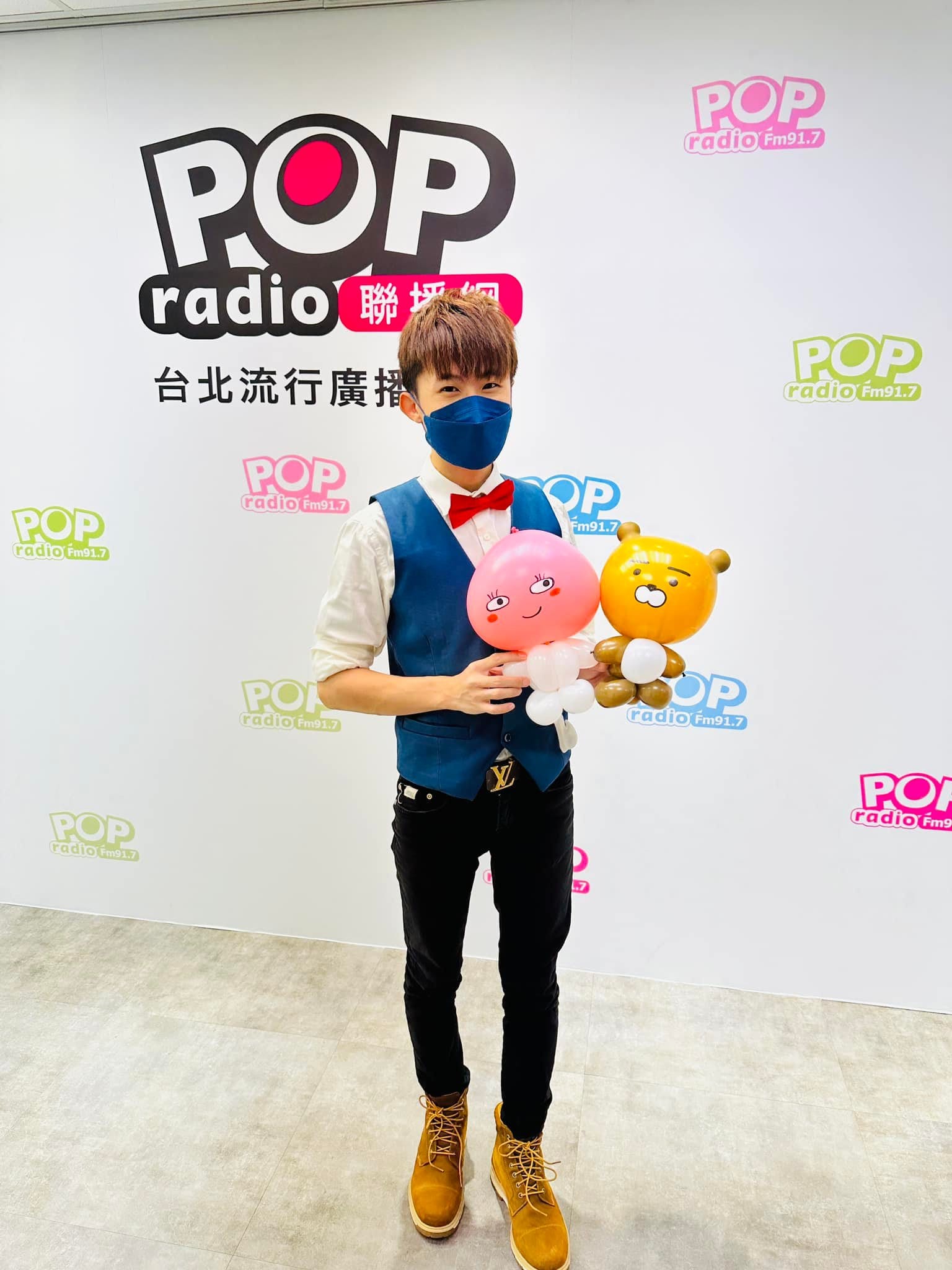 柯男在 POP Radio 背板前，手捧黃色小熊與粉紅桃子造型氣球