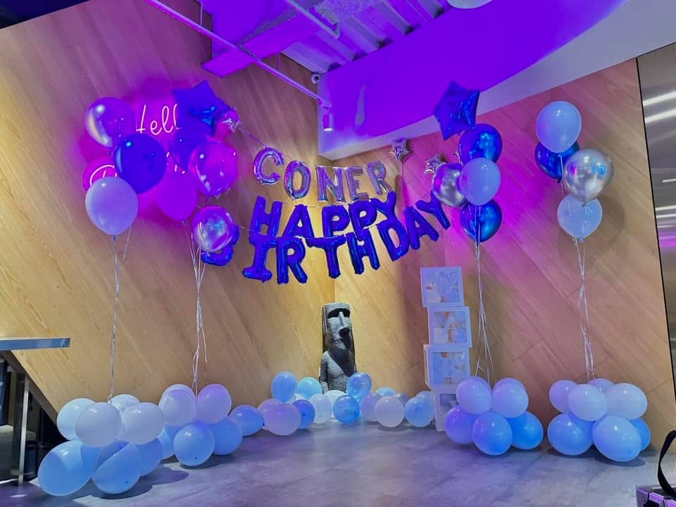 木紋牆上的深藍 HAPPY BIRTHDAY 字母氣球與銀色 CONER 名字氣球，兩側藍紫銀空飄氣球束，地面淺藍白氣球堆，紫色燈光照亮