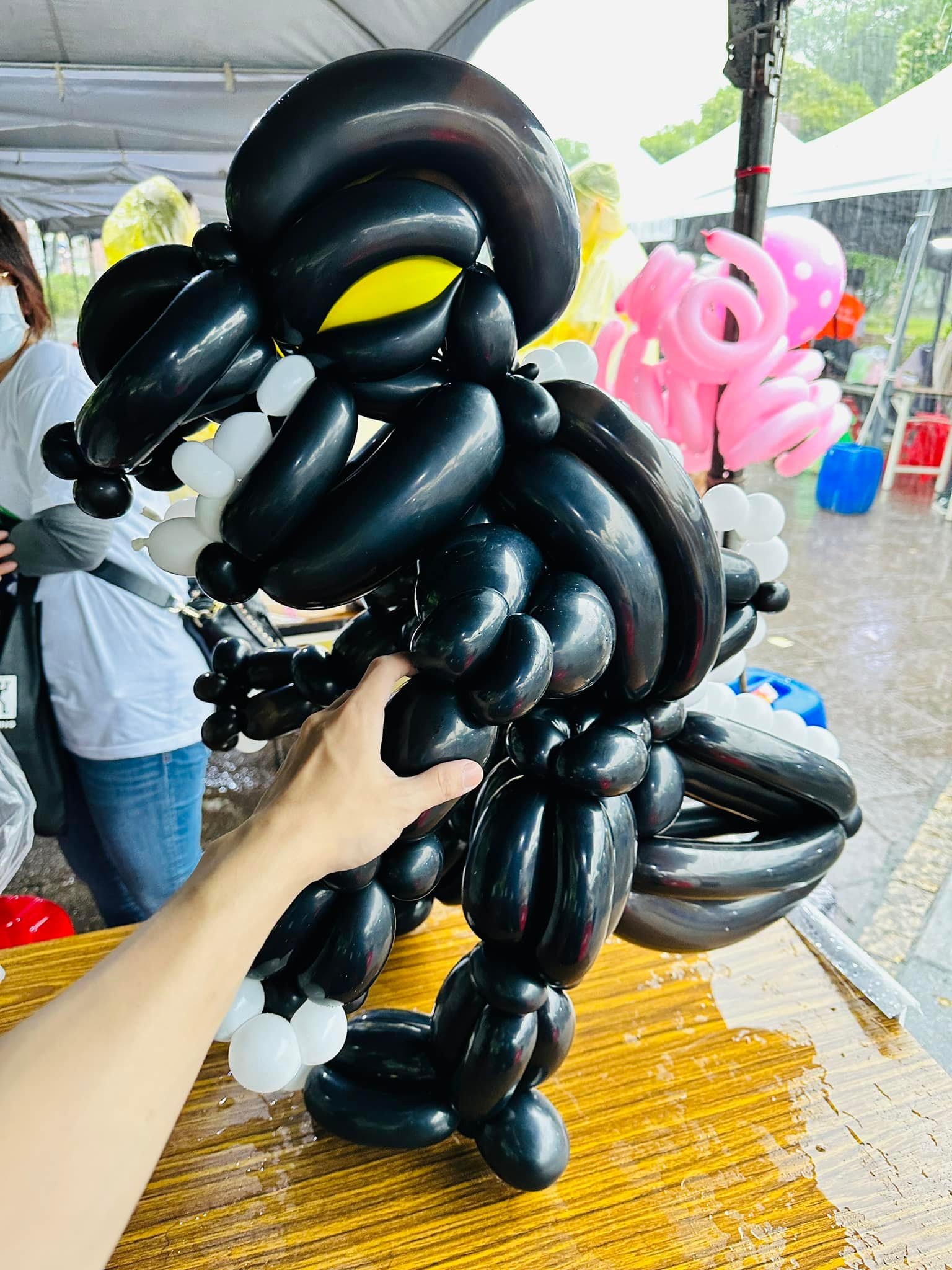 黑色哥吉拉造型氣球特寫，黃色眼睛、白色尖牙，背上一排白色背鰭，後面下著大雨