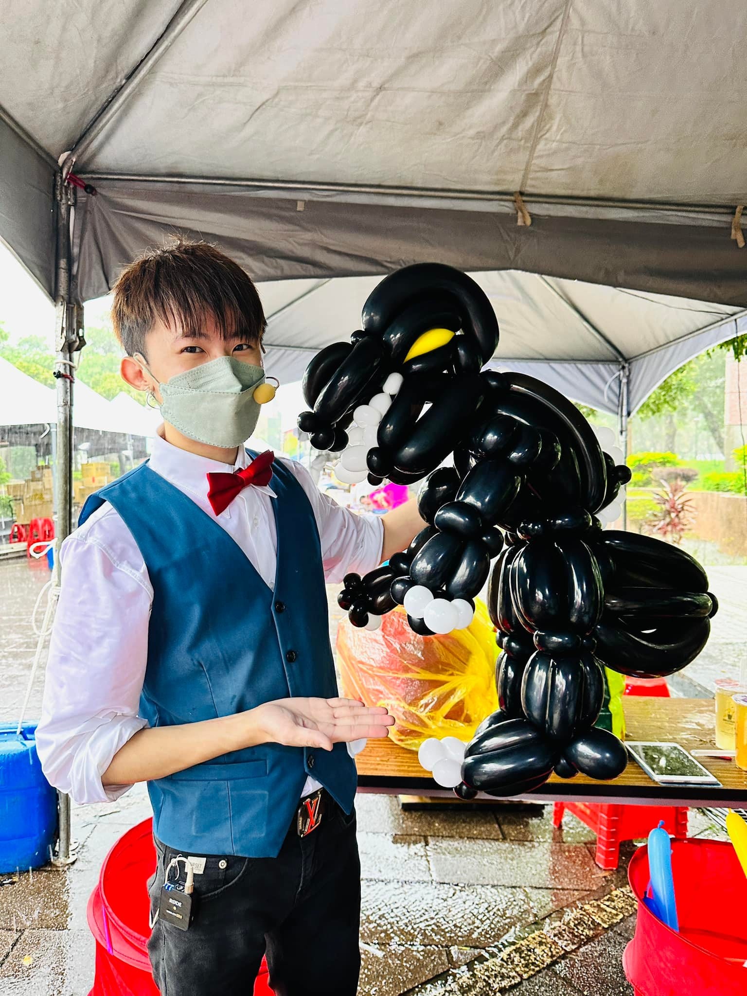 雨中的白色帳篷下，我戴口罩站在桌邊，旁邊是一隻跟我上半身一樣大的黑色哥吉拉造型氣球