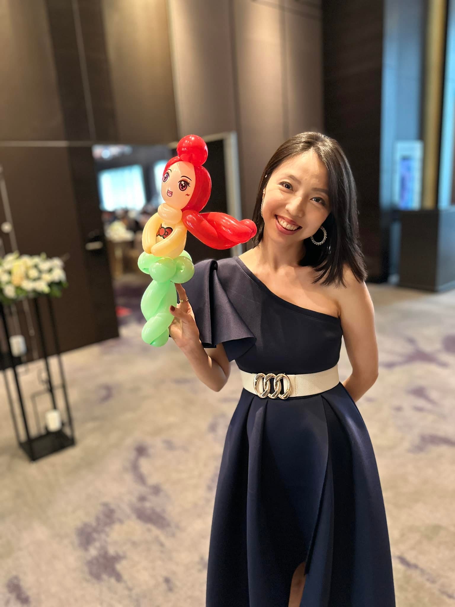 穿深藍禮服的女賓客拿著紅髮綠尾巴的小美人魚造型氣球微笑