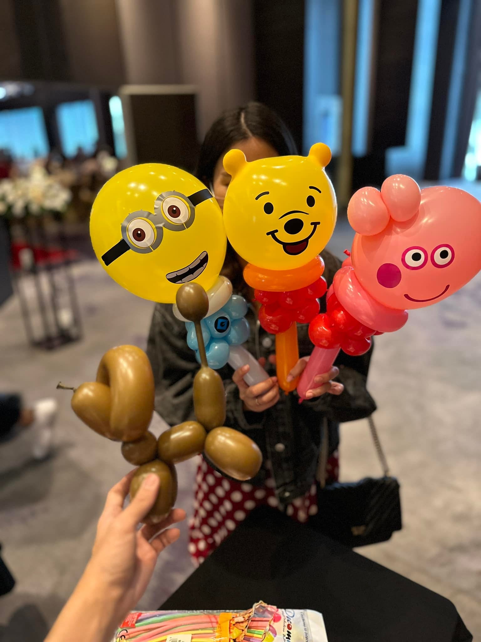 賓客手上拿著小小兵、小熊維尼、佩佩豬三支手持氣球，前方還有一隻咖啡色小狗氣球