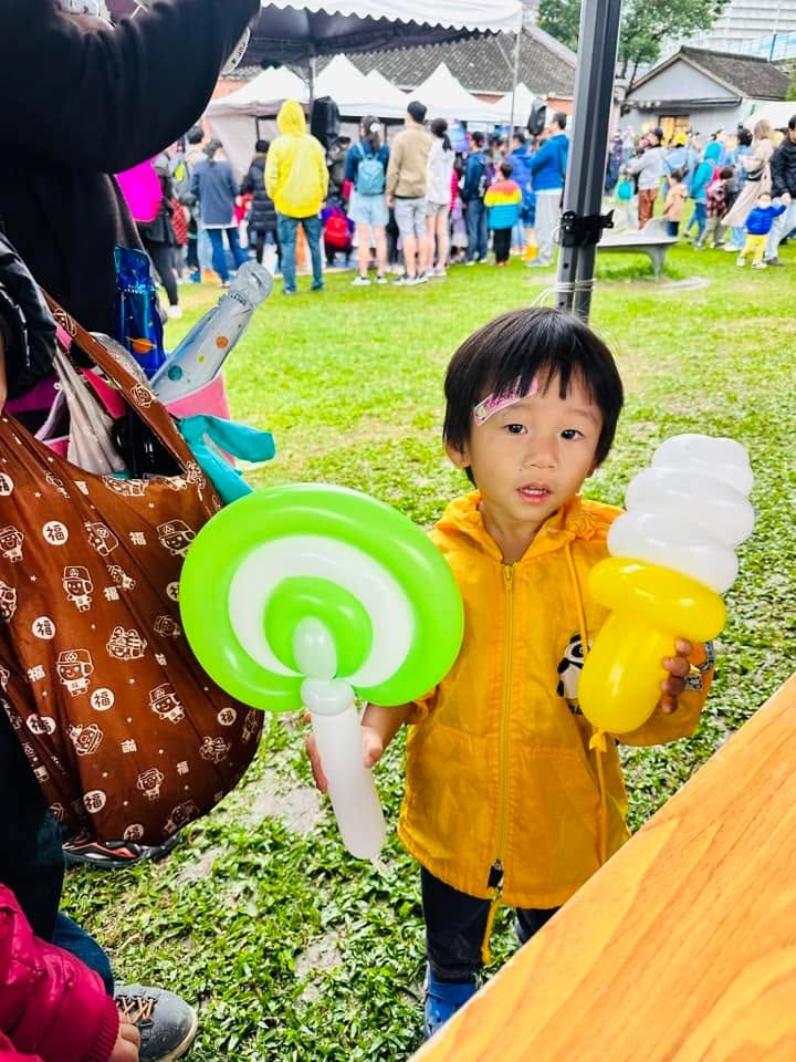 穿黃色雨衣的小男孩一手拿綠白棒棒糖氣球、一手拿黃白冰淇淋氣球