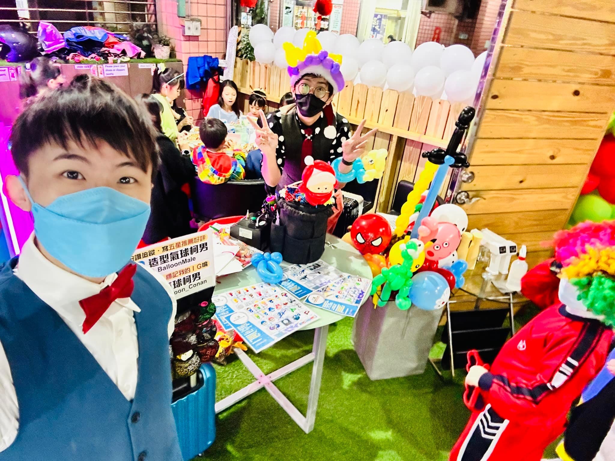 柯男自拍，後方戴紫色氣球帽的表演者比 YA，桌上放著蜘蛛人等造型氣球