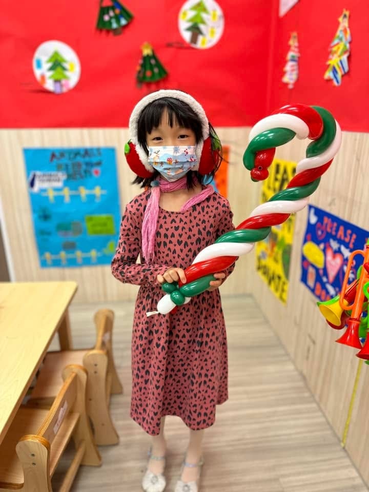 戴耳罩的小女孩抱著紅白綠三色的大型拐杖糖氣球