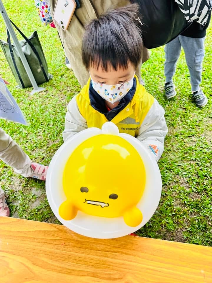 小男孩低頭看著懶洋洋表情的蛋黃哥造型氣球，白色蛋白托著黃色蛋黃