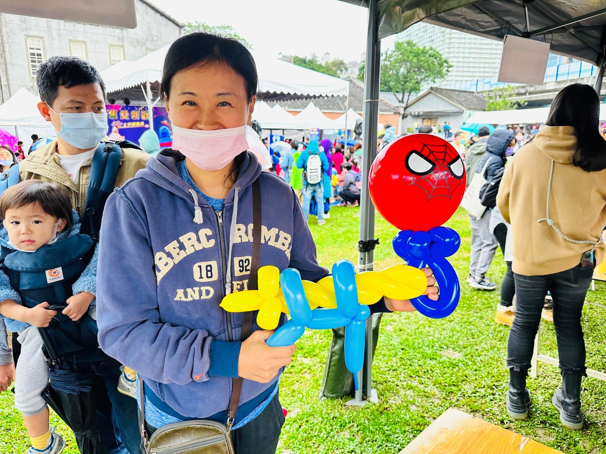 台北華山戶外活動，媽媽拿著蜘蛛人頭氣球棒和黃藍色氣球劍站在帳篷旁