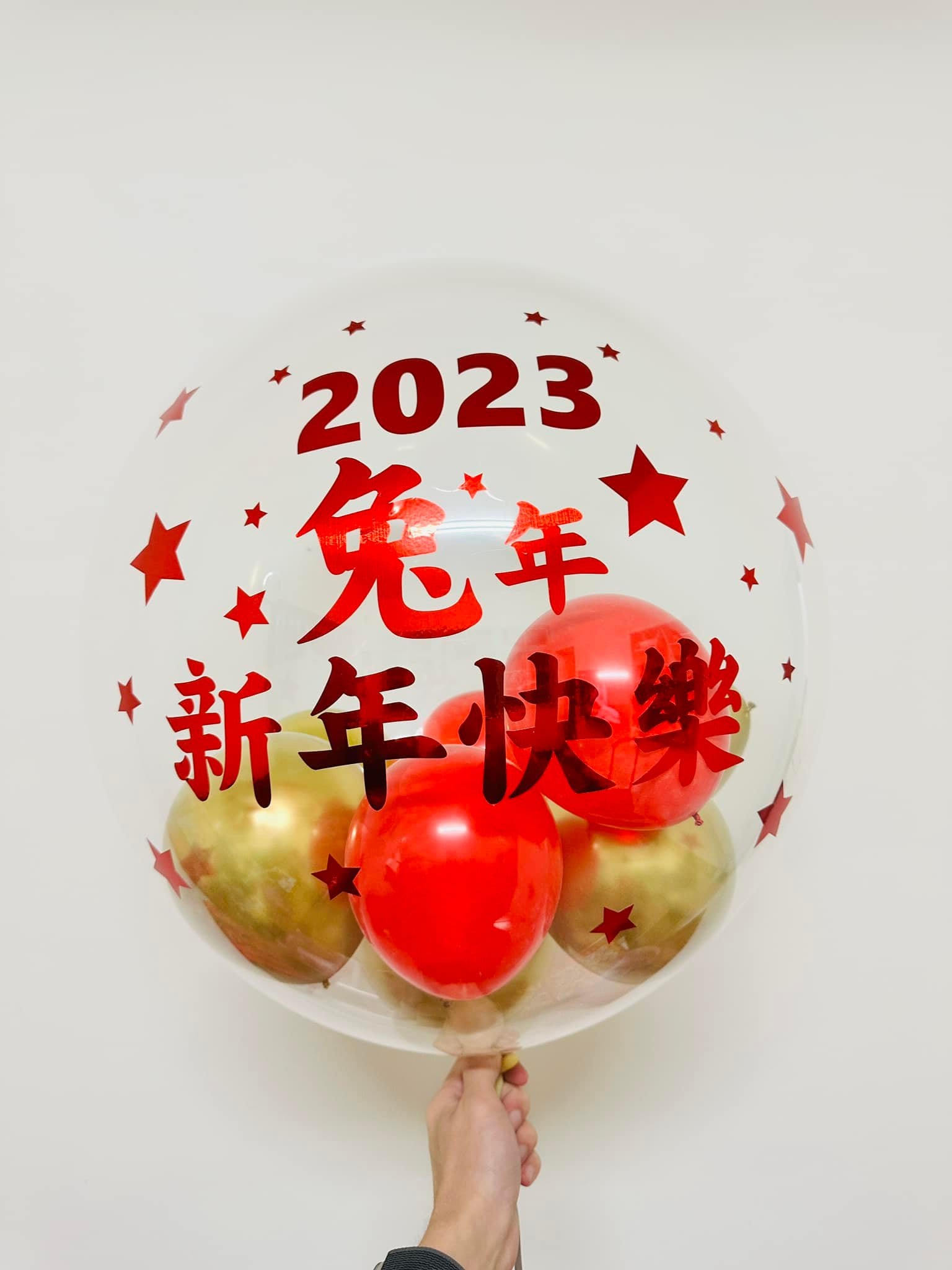 透明波波球上用紅字寫著 2023 兔年新年快樂，周圍點綴紅色星星，裡面裝紅色與金色小氣球