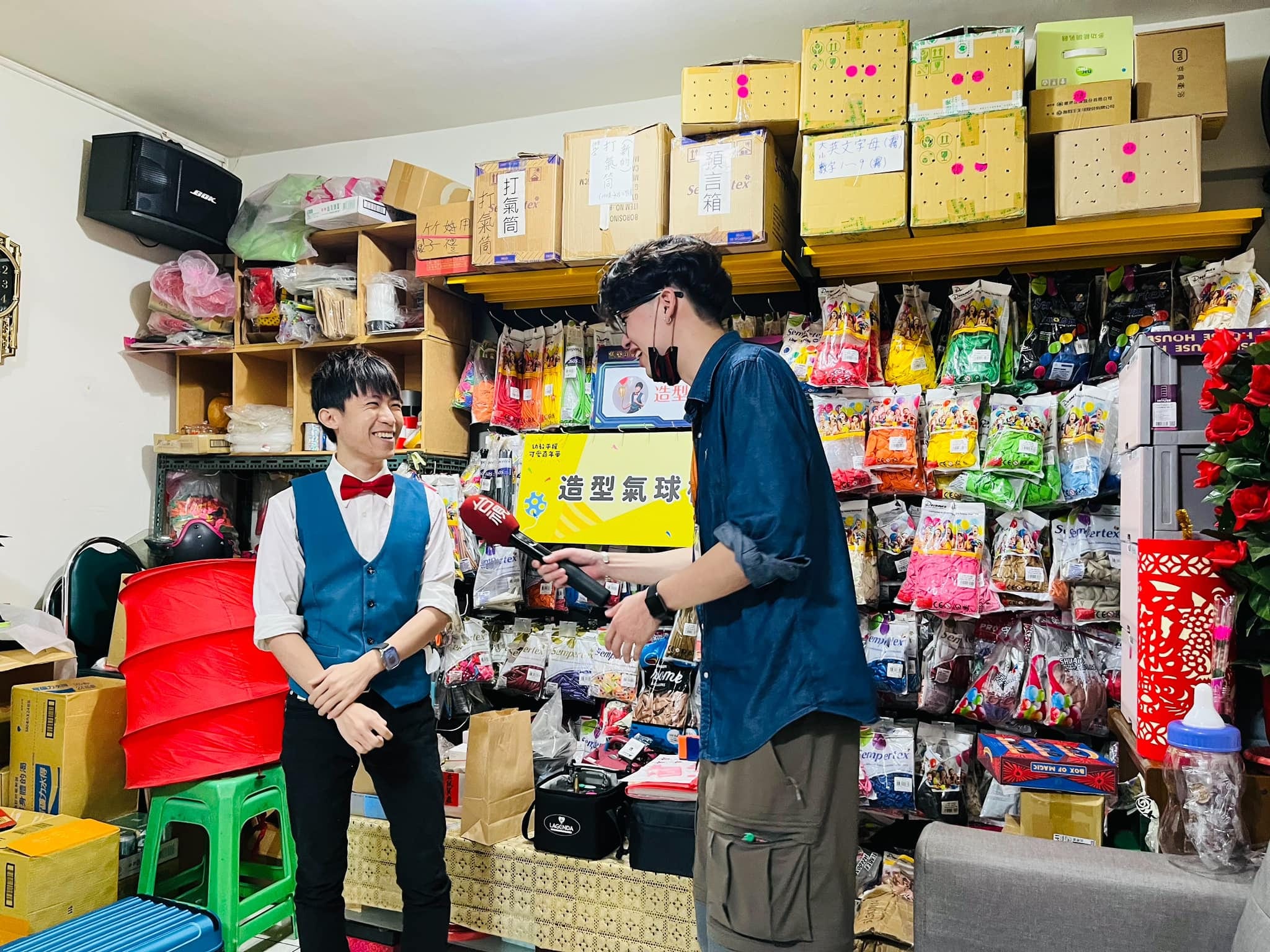 記者在貨架前拿手機拍攝，柯男站在一旁說明
