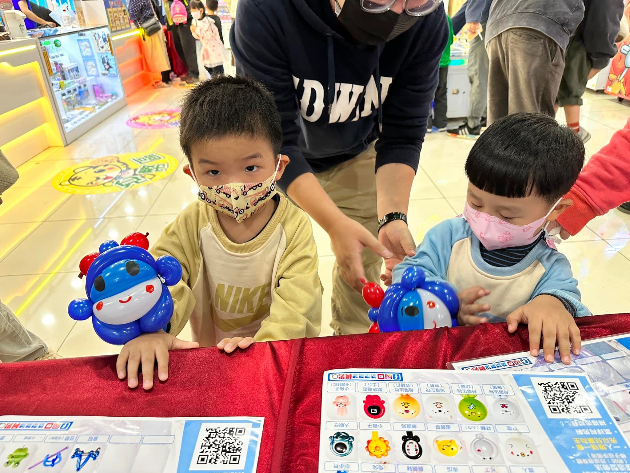 兩個幼兒趴在桌邊，各拿一台頭頂紅燈的藍色車子造型氣球