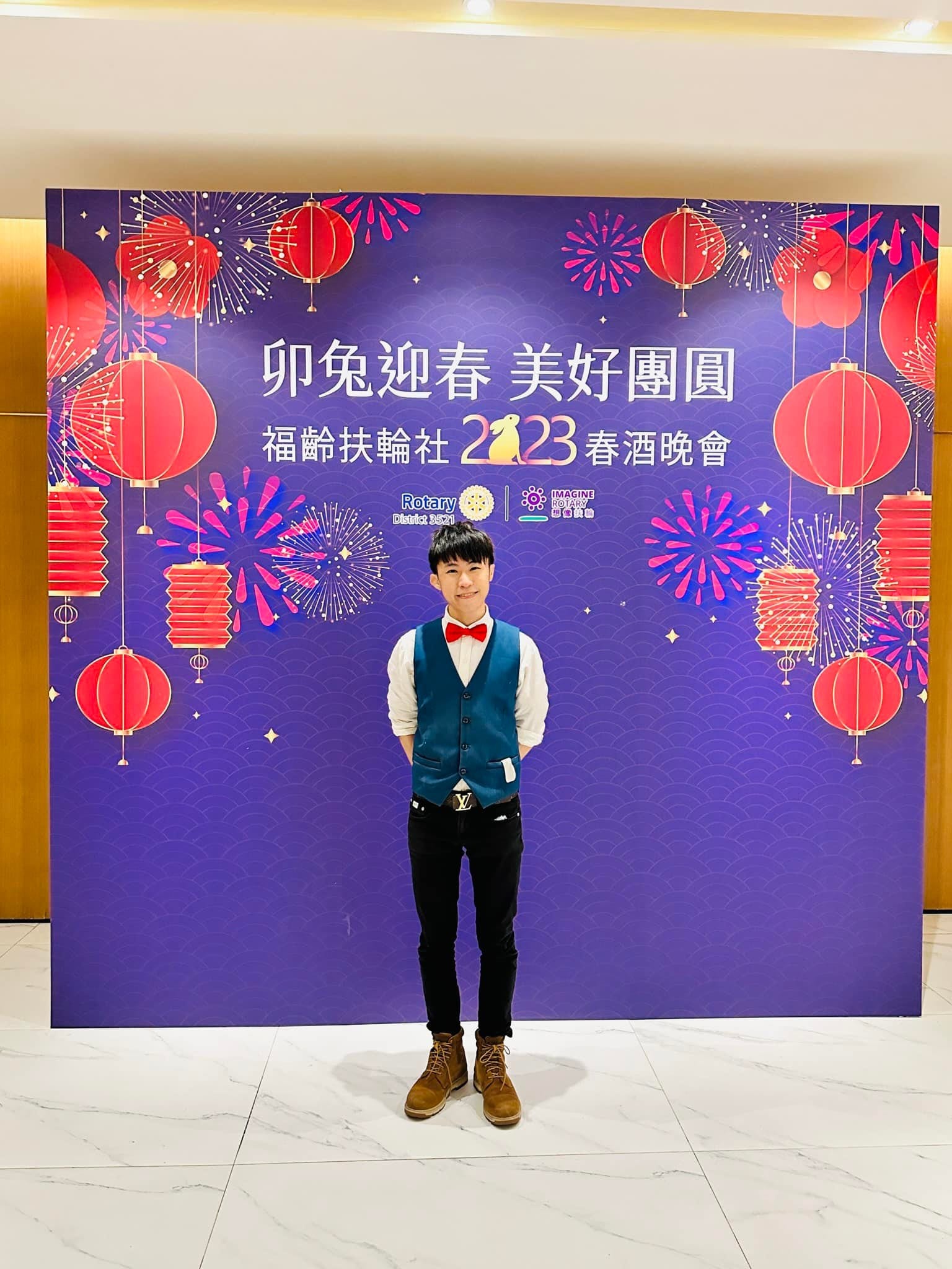 柯男站在紫色兔年春酒背板前，背板上有紅燈籠與煙火圖案