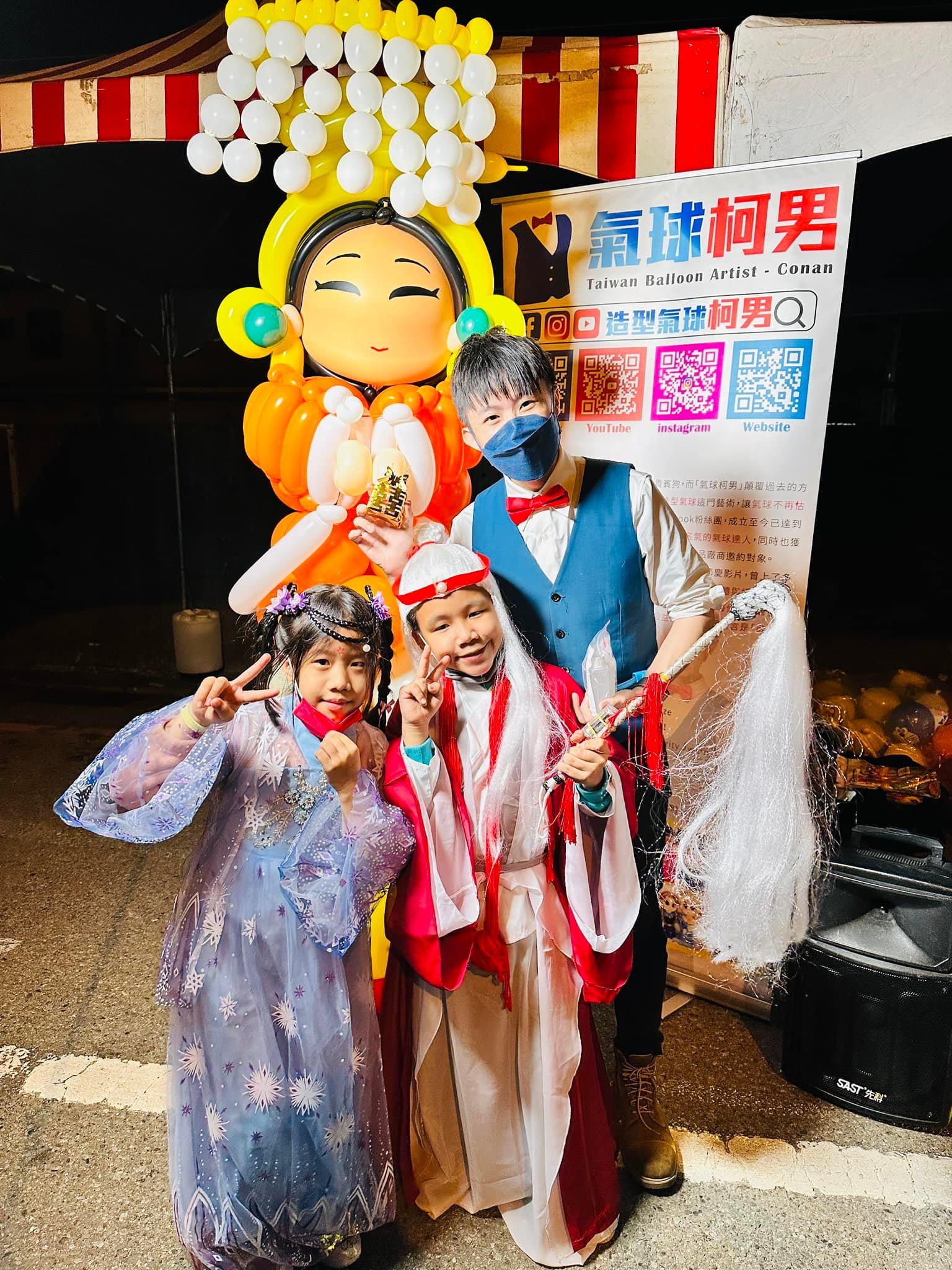 兩個穿古裝的孩子拿著拂塵，在媽祖氣球前和柯男合影
