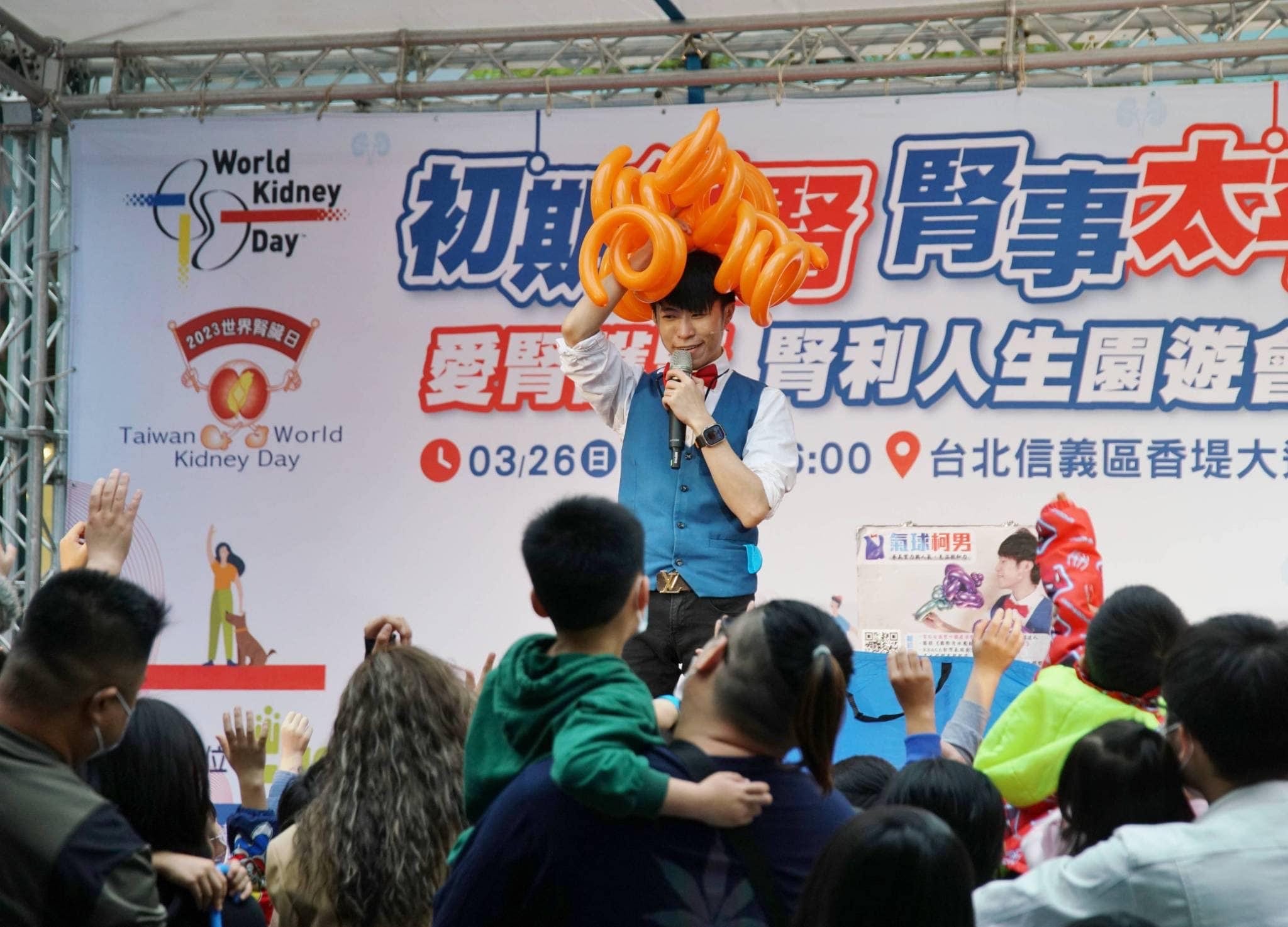 柯男頭戴橘色章魚腳造型氣球帽，拿麥克風表演