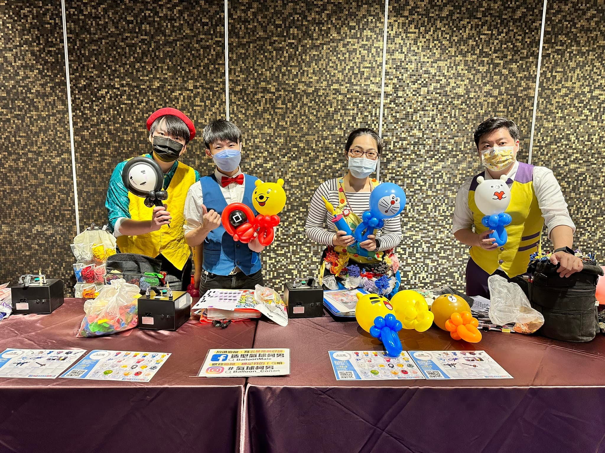 台中春酒會場，四位氣球達人各拿一隻造型氣球站在攤位後合照