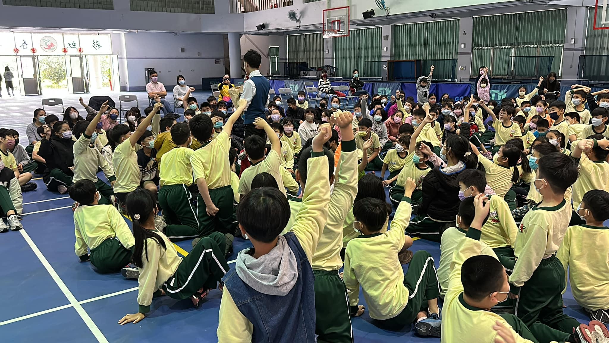 學生坐在活動中心地板上踴躍舉手，爭取上台當魔術助手
