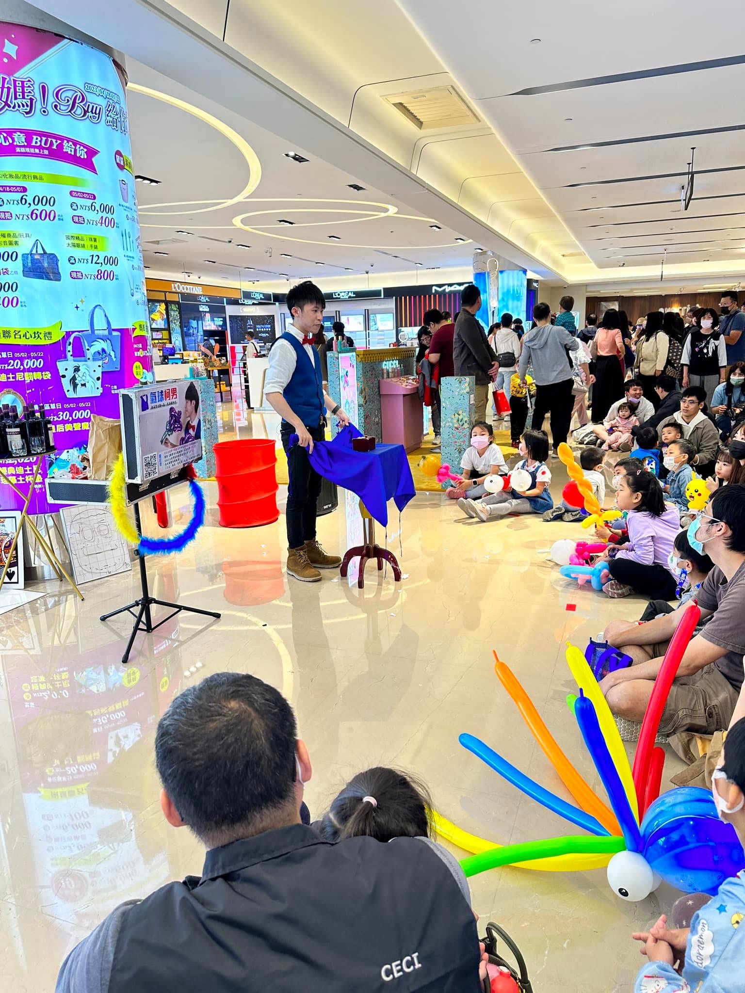 魔術桌旁的觀眾群，前排孩子抱著彩色章魚氣球