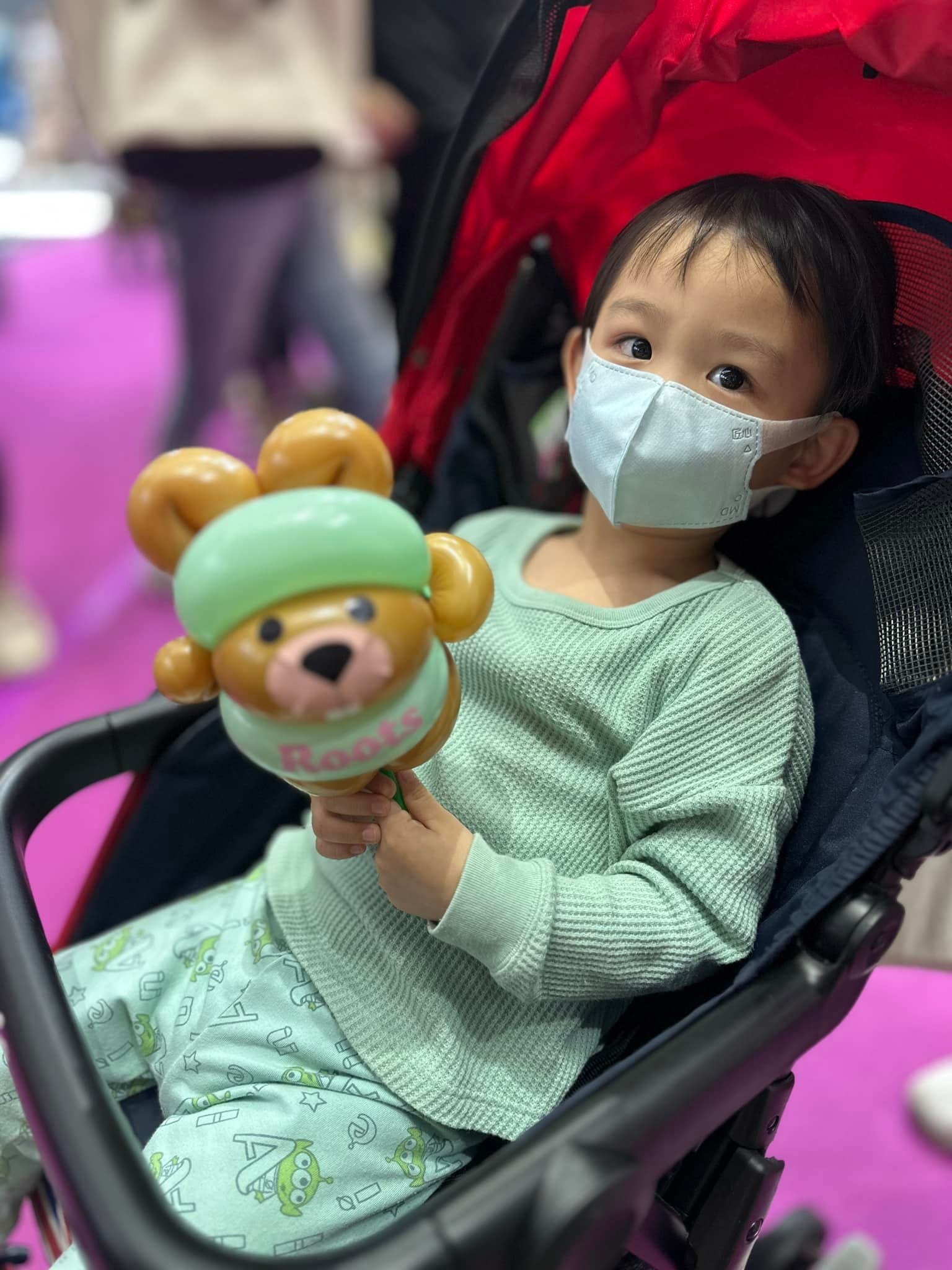 坐在推車上的幼童拿著薄荷綠海狸寶寶氣球，衣服顏色剛好同色