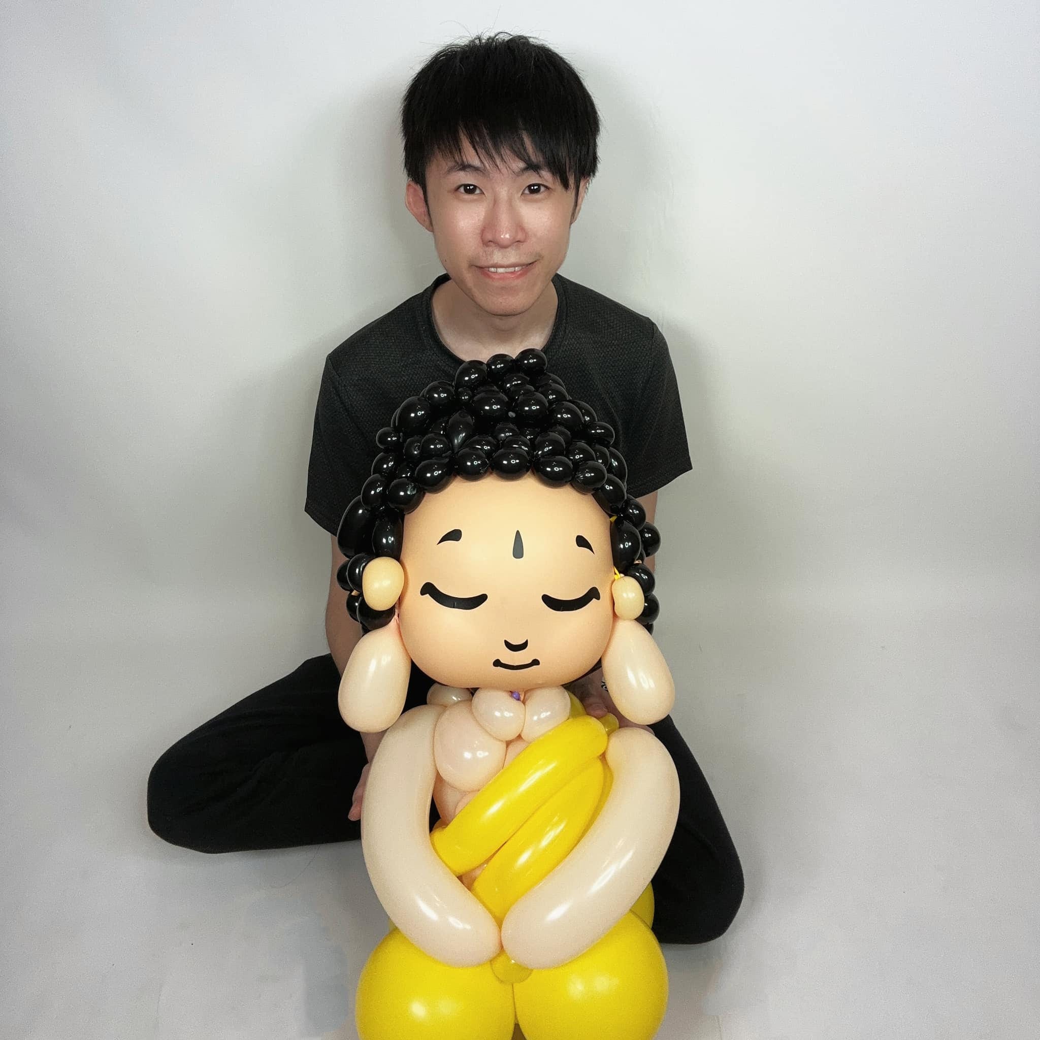 柯男坐在白色背景前，抱著完成的釋迦牟尼佛氣球人偶