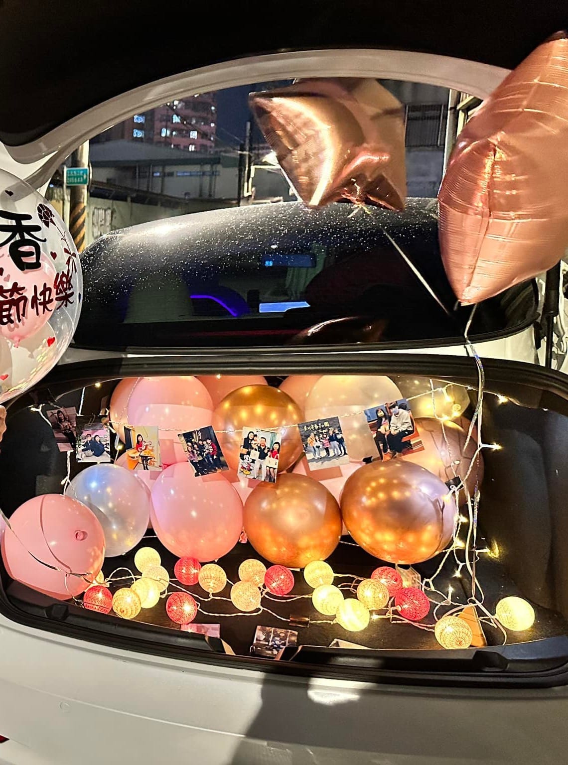 後車廂內夾著全家照片的燈串,下方鋪滿粉色、香檳金氣球與彩色棉球燈