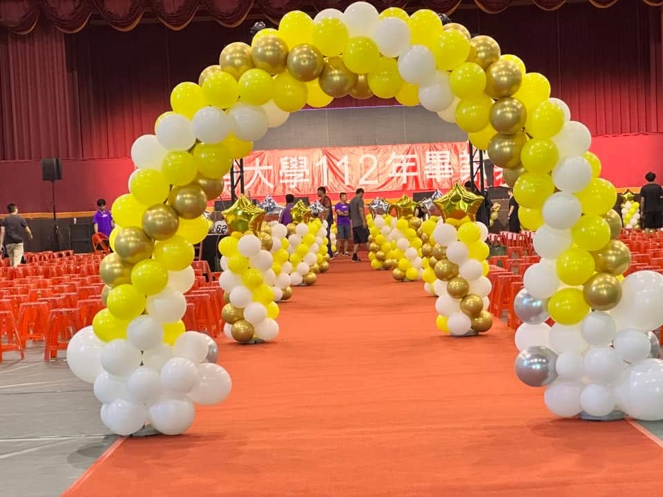 2023 年 6 月畢業典禮，黃白金色氣球拱門跨在紅地毯上，後方排著氣球柱