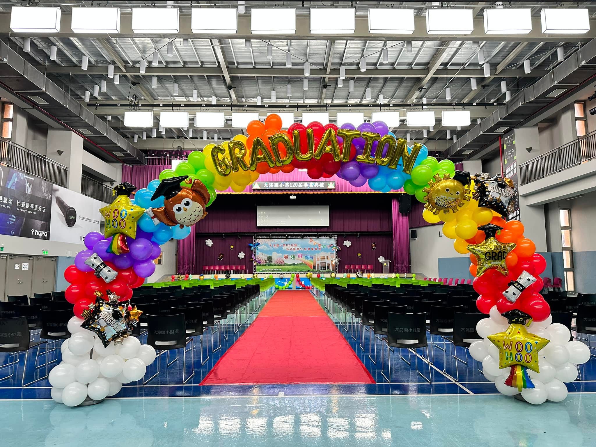 桃園大溪國小禮堂畢業典禮佈置，彩虹氣球拱門掛金色 GRADUATION 字母，中間鋪紅地毯