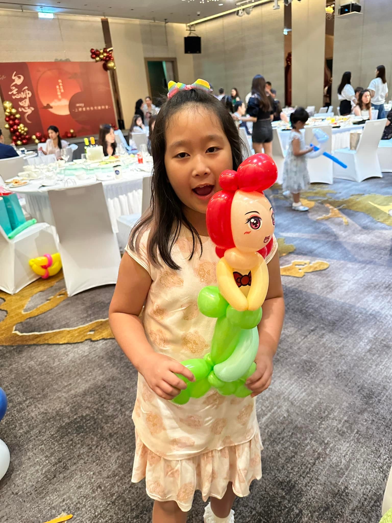 女孩拿著紅髮、綠色魚尾的小美人魚造型氣球，在宴會廳開心張嘴笑