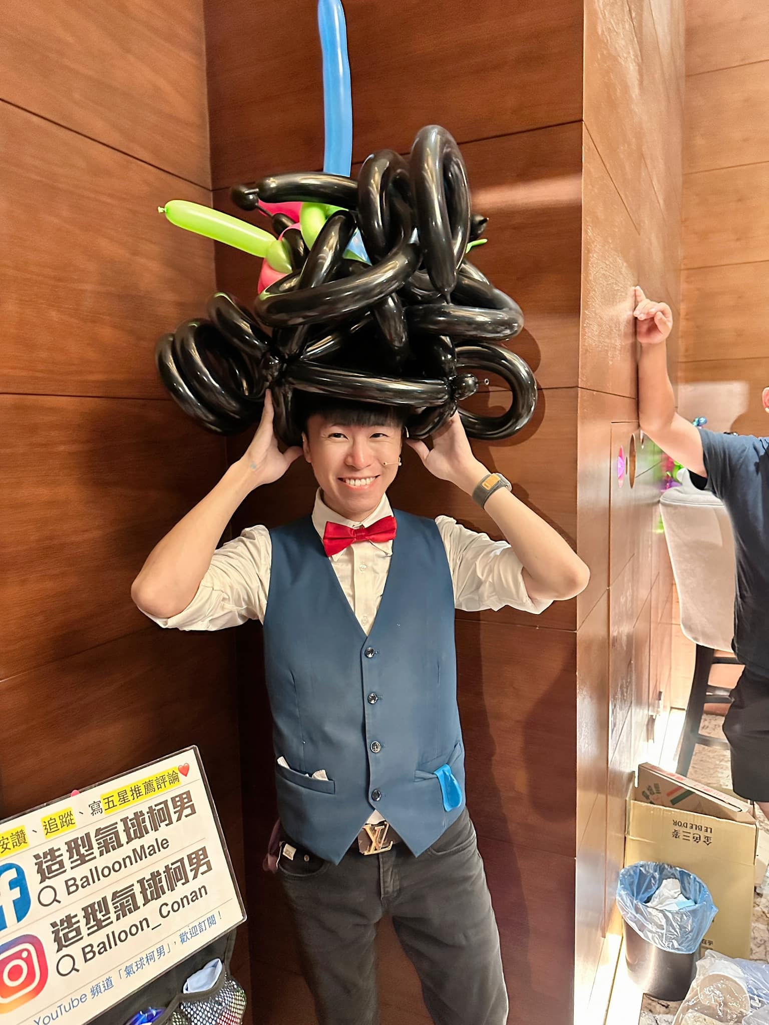 柯男頭戴黑色捲髮造型的氣球帽,雙手扶著帽子大笑