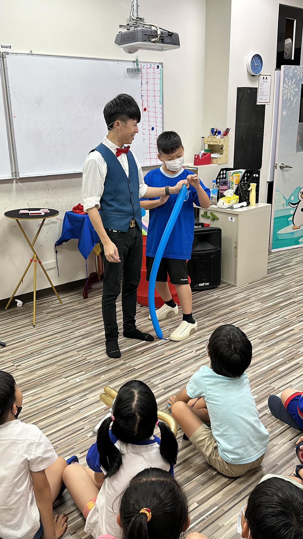 安親班教室裡，柯男和戴口罩的男孩一起拉著藍色長條氣球表演