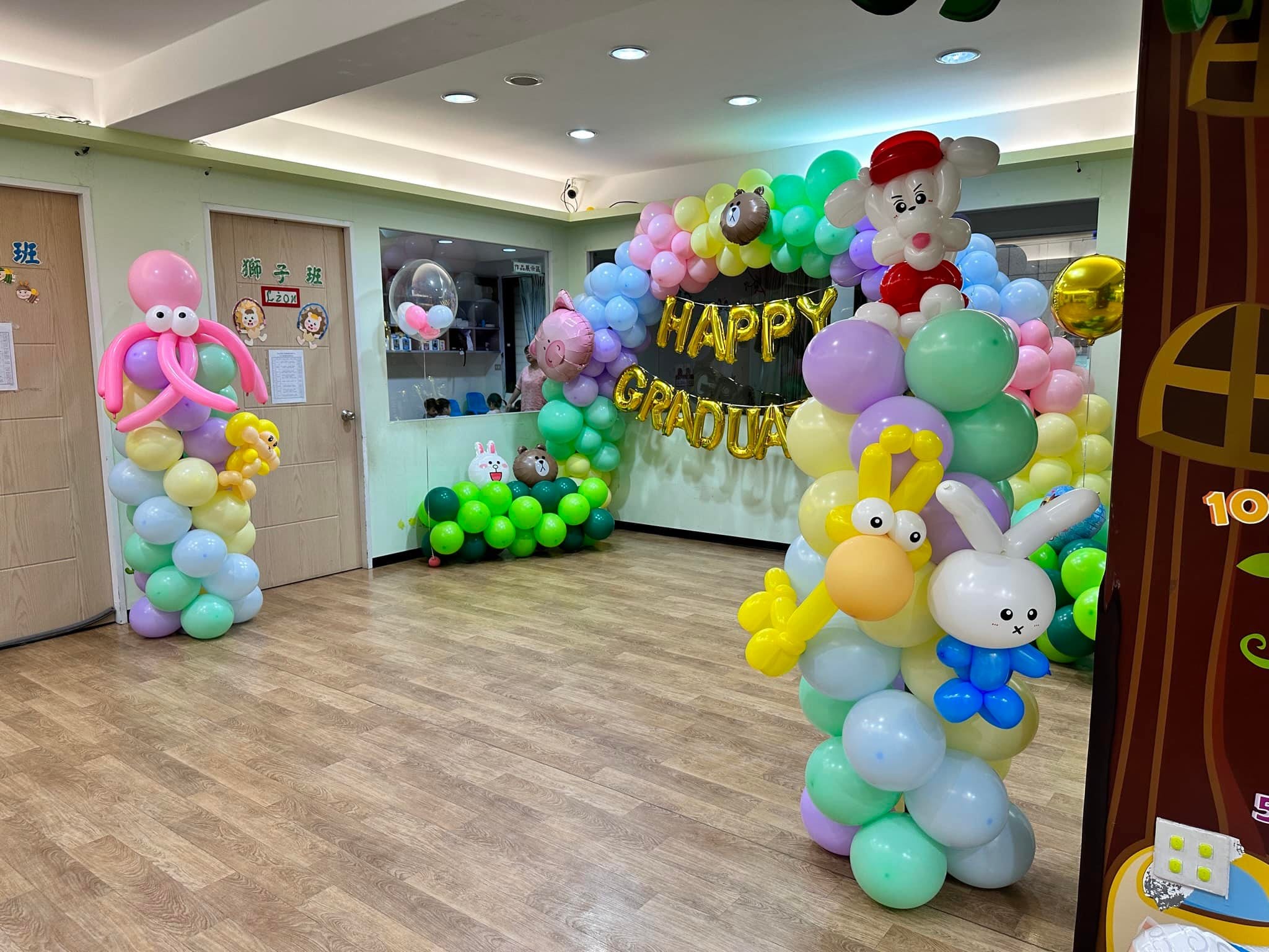 幼兒園大廳全景，粉彩氣球柱頂端是戴紅帽的白兔造型，後方是畢業拱門