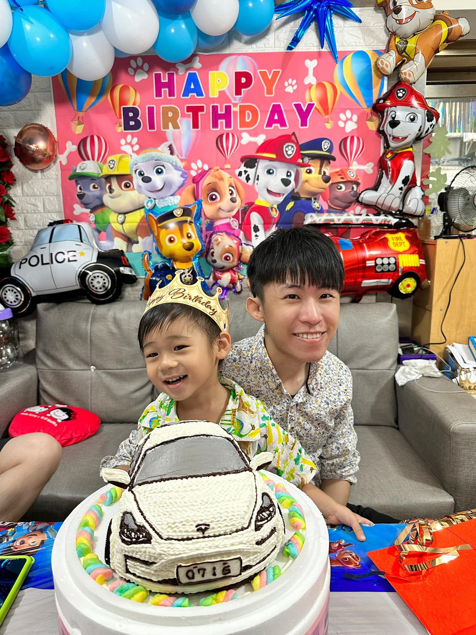 戴生日皇冠的外甥和我坐在汪汪隊背板前，前方是白色特斯拉造型蛋糕