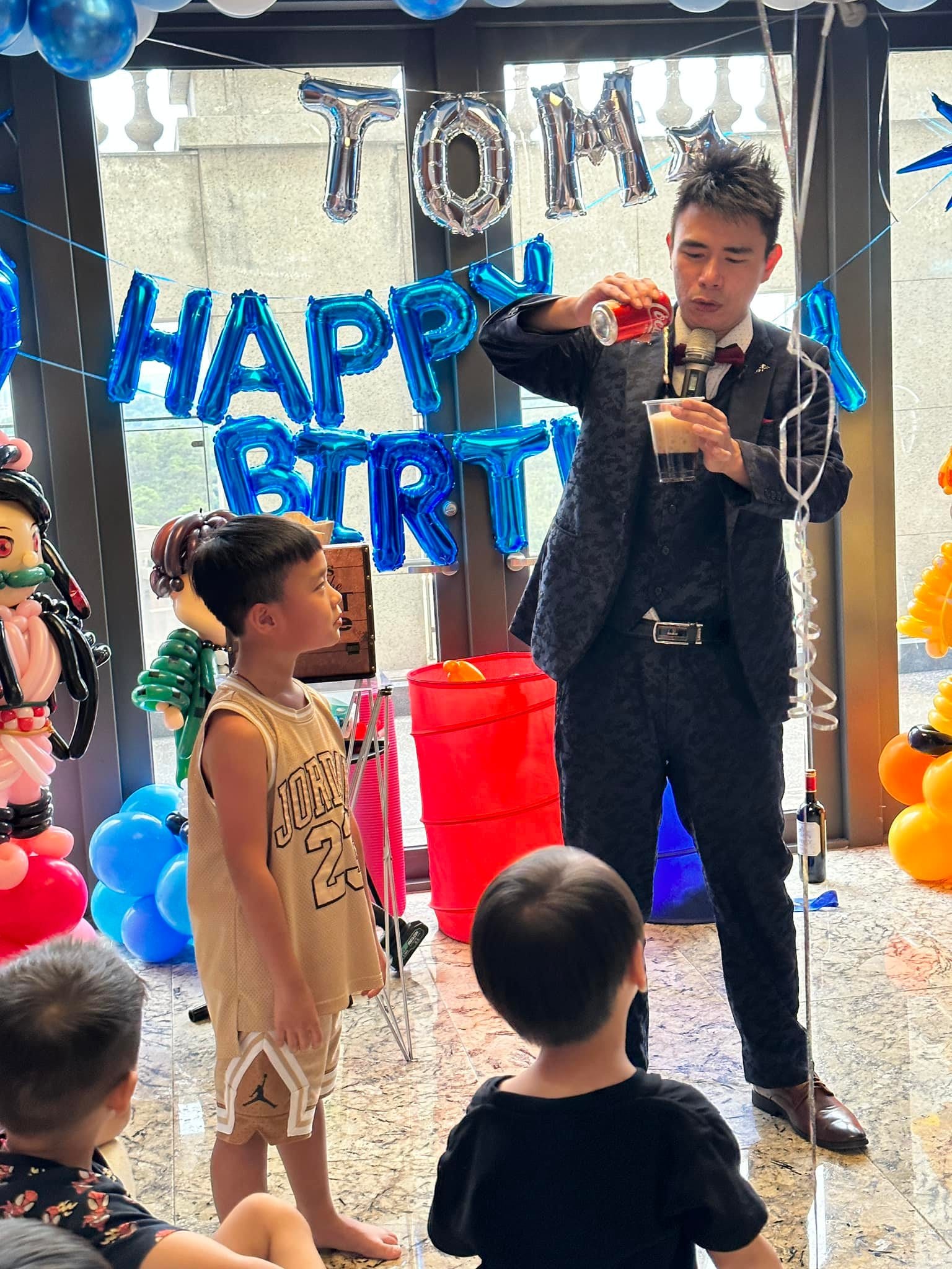 團隊魔術師在生日背板前表演倒飲料魔術,孩子們站在前面看