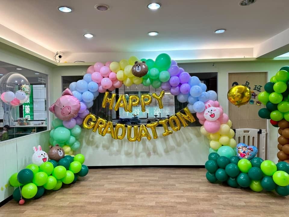 幼兒園畢業佈置，彩虹色氣球拱門掛著金色 HAPPY GRADUATION 字母與熊大、兔兔鋁箔氣球