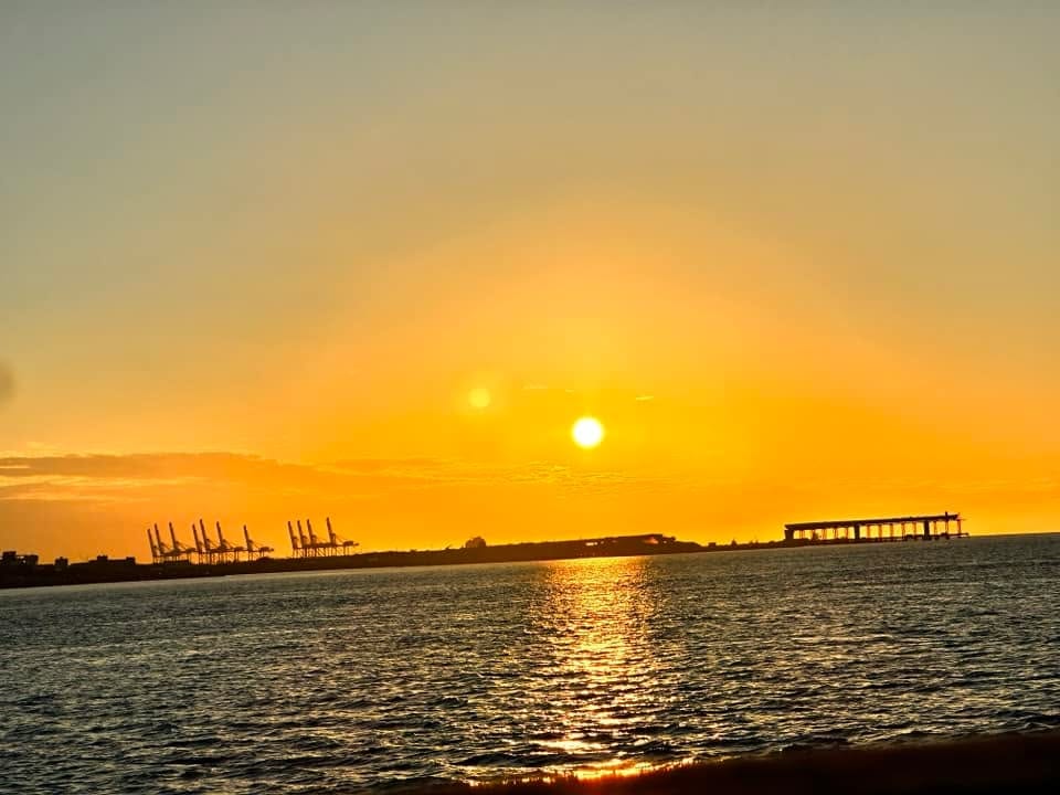 遊艇航程中看到的金黃色夕陽，遠方是港口的吊臂與海面倒影