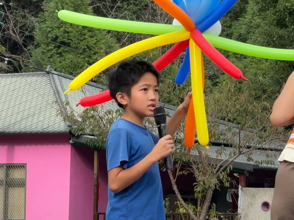 穿藍色上衣的男孩拿著麥克風發表心得，頭上舉著彩虹章魚造型氣球