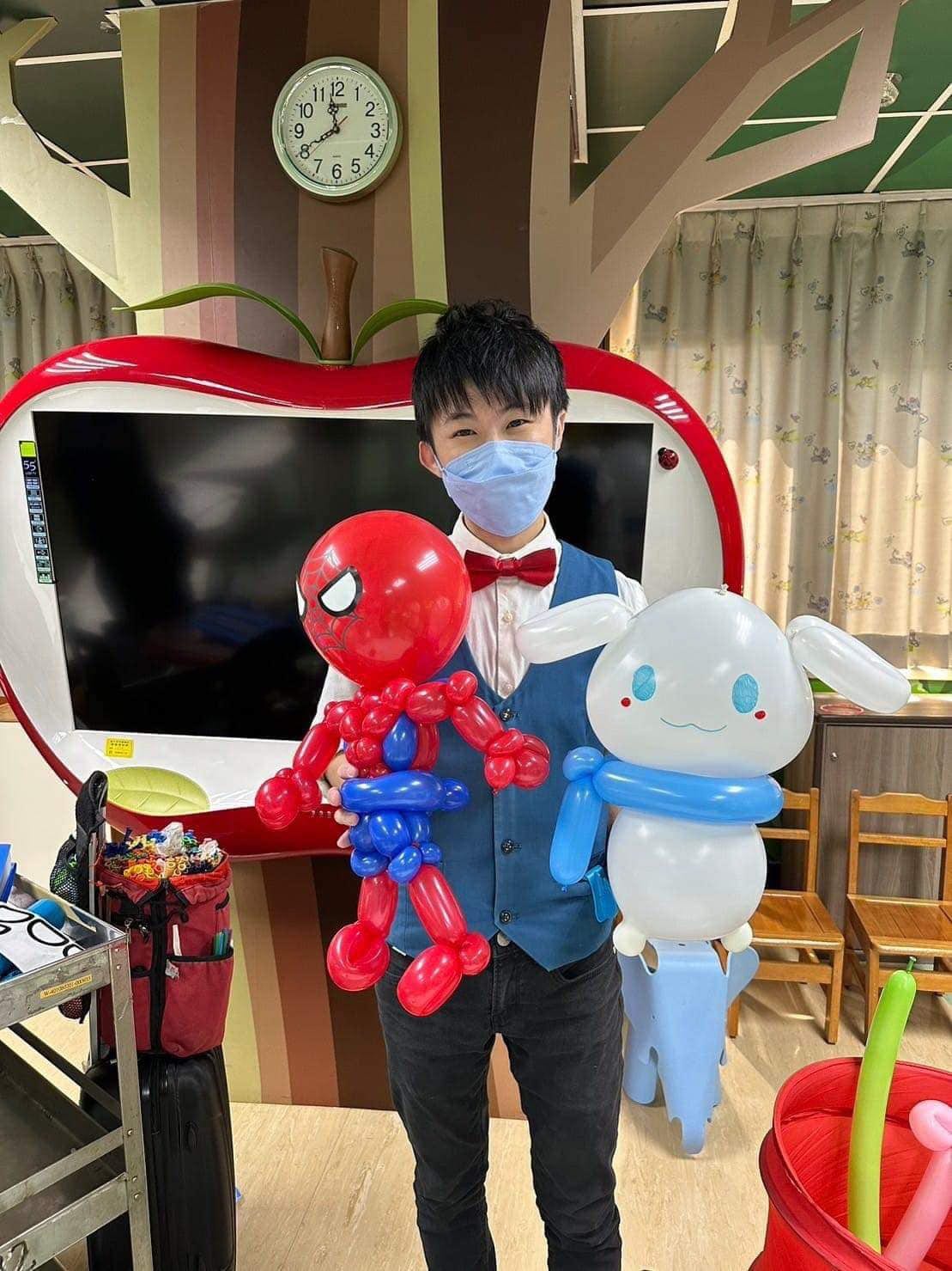 柯男在榮總兒童病房遊戲室，雙手拿著蜘蛛人與大耳狗喜拿造型氣球